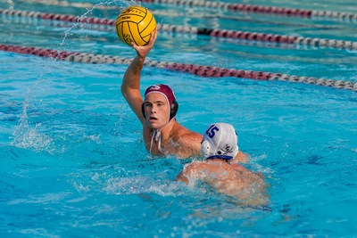 Men's waterpolo player looking to pass ball against defender.